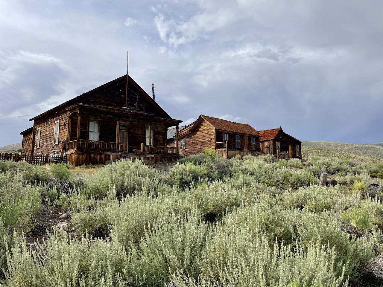 Weathered wooden buildings of an old ghost town surrounded by sagebrush under a cloudy sky