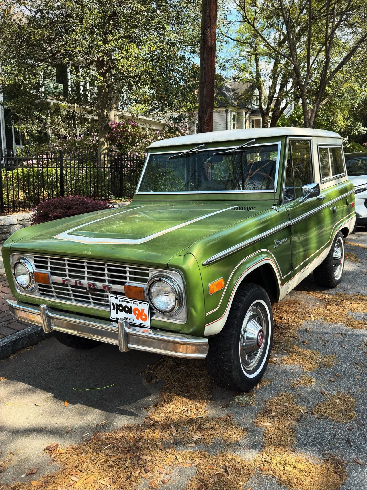 A green vintage Ford Bronco with a white roof parked on a residential street, three-quarter front view.