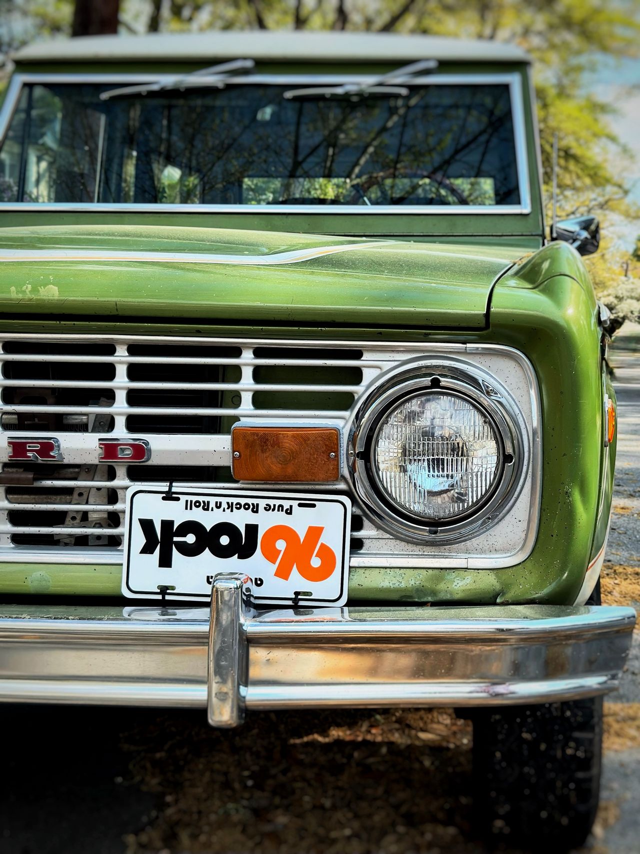 Close-up of the front of a green vintage Ford Bronco showing a '96 rock—Pure Rock'n'Roll' vanity plate and chrome grille.