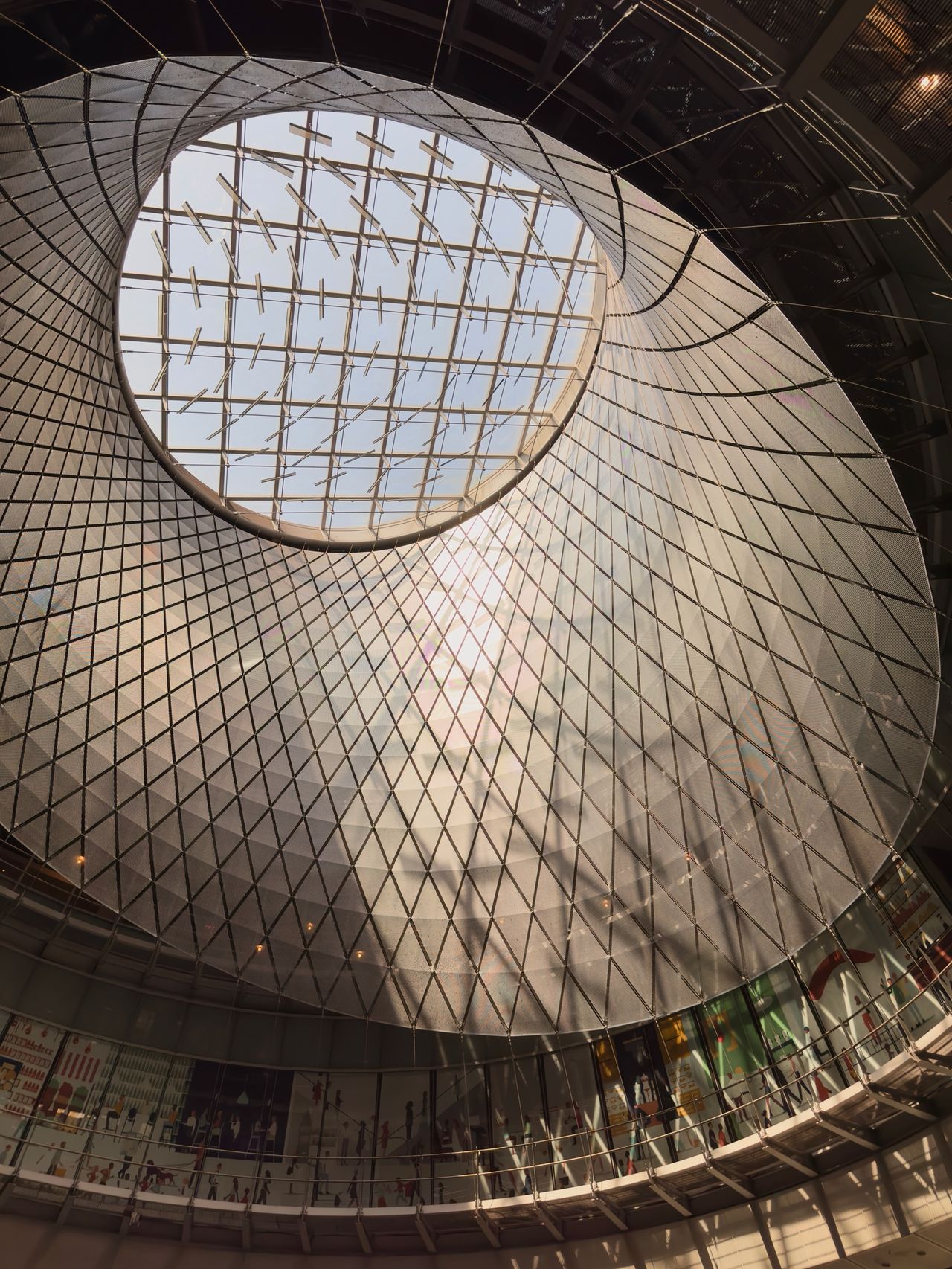 Looking up through a circular atrium skylight with a suspended geometric installation.
