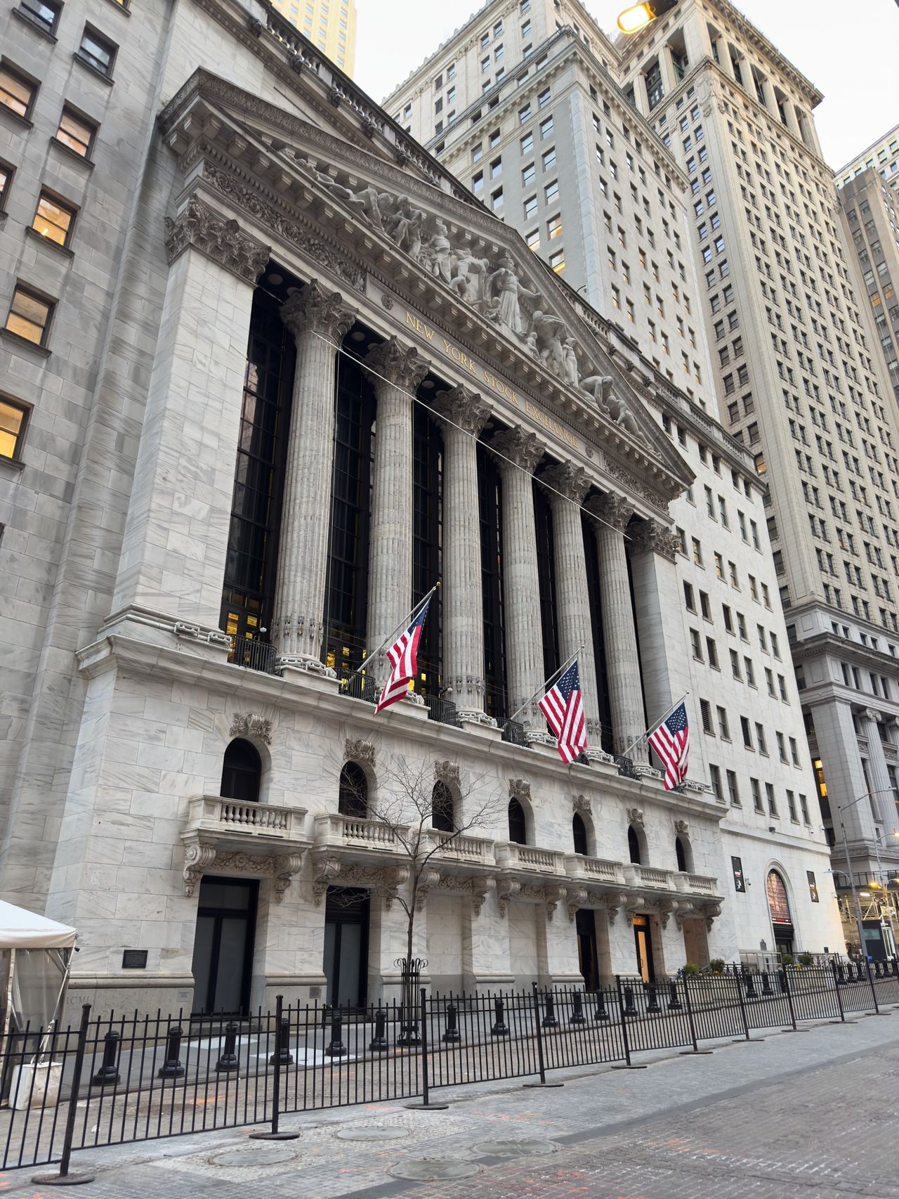 The columned classical facade of the New York Stock Exchange with three American flags hanging between the columns.