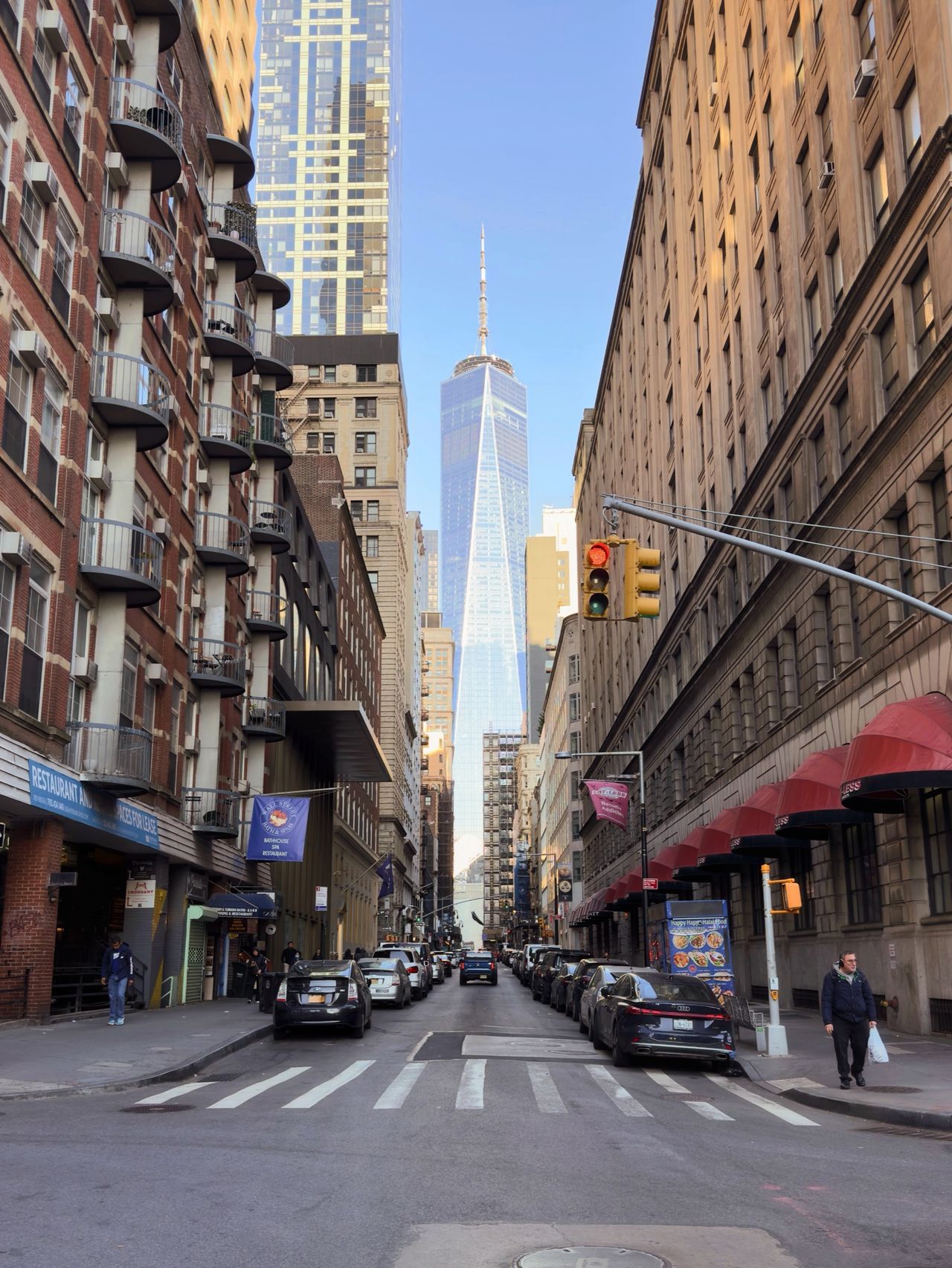 One World Trade Center stands at the end of a narrow street lined with brownstones and storefront awnings.