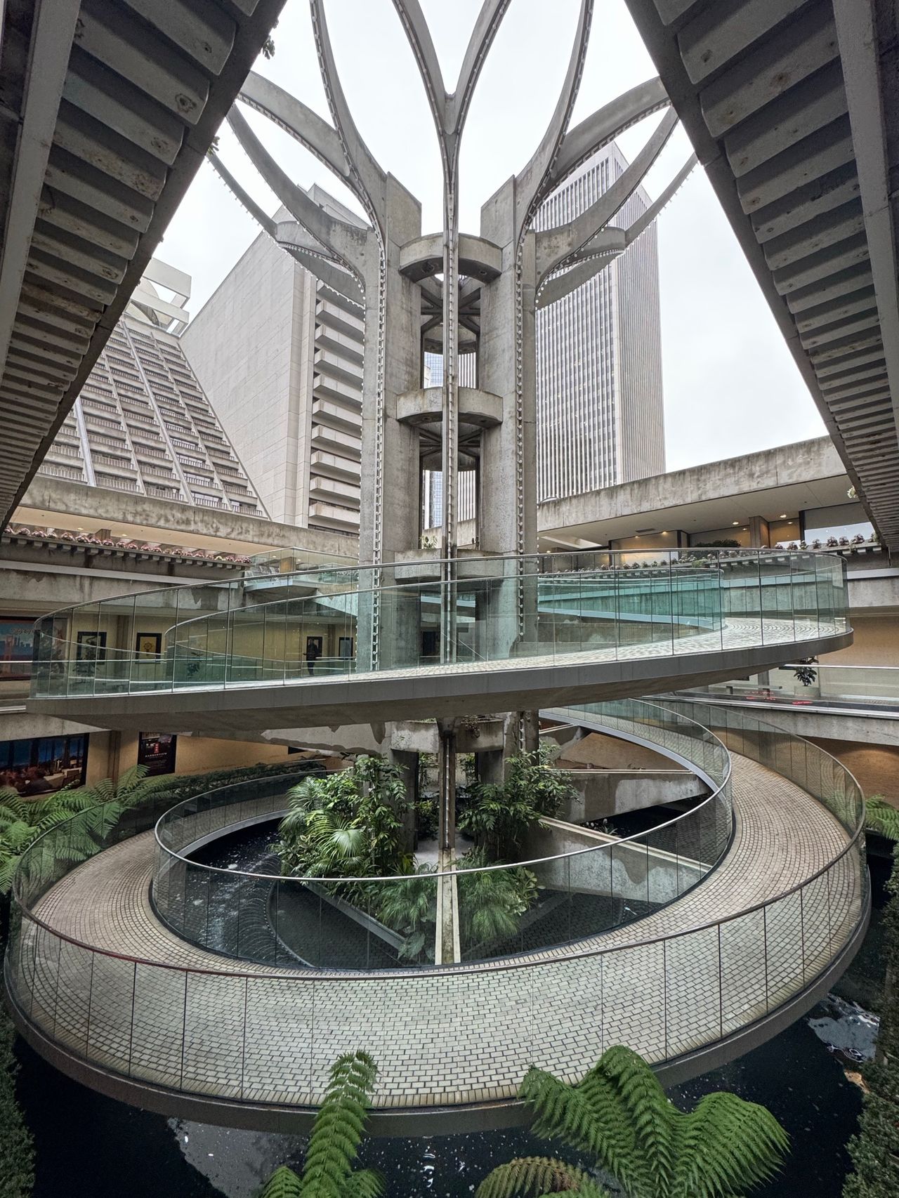 The atrium at 4 Embarcadero Center with its cylindrical glass-walled elevator core, curved walkways, and a central planted circle below.