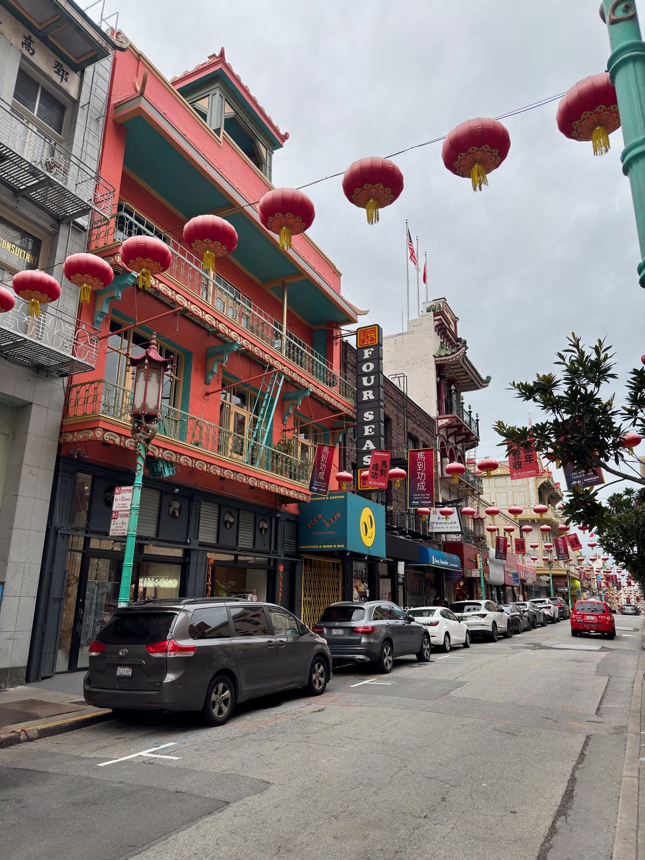 A Chinatown street strung with rows of red paper lanterns and a 'FOUR SEAS' restaurant sign above colorful storefronts.