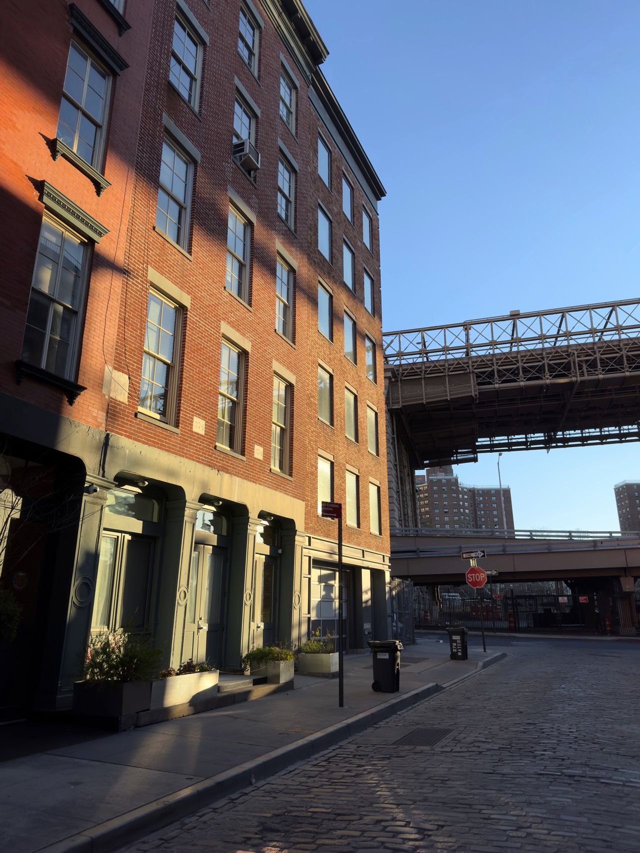 A historic red-brick loft on a cobblestone street, with a steel truss bridge crossing overhead in the distance.