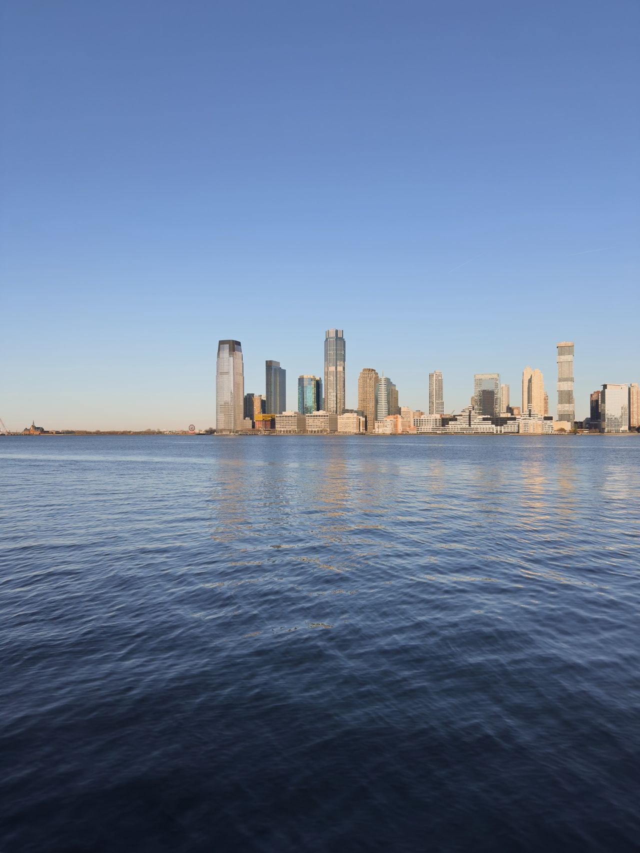 Jersey City skyline rises across the calm Hudson River under a clear morning sky