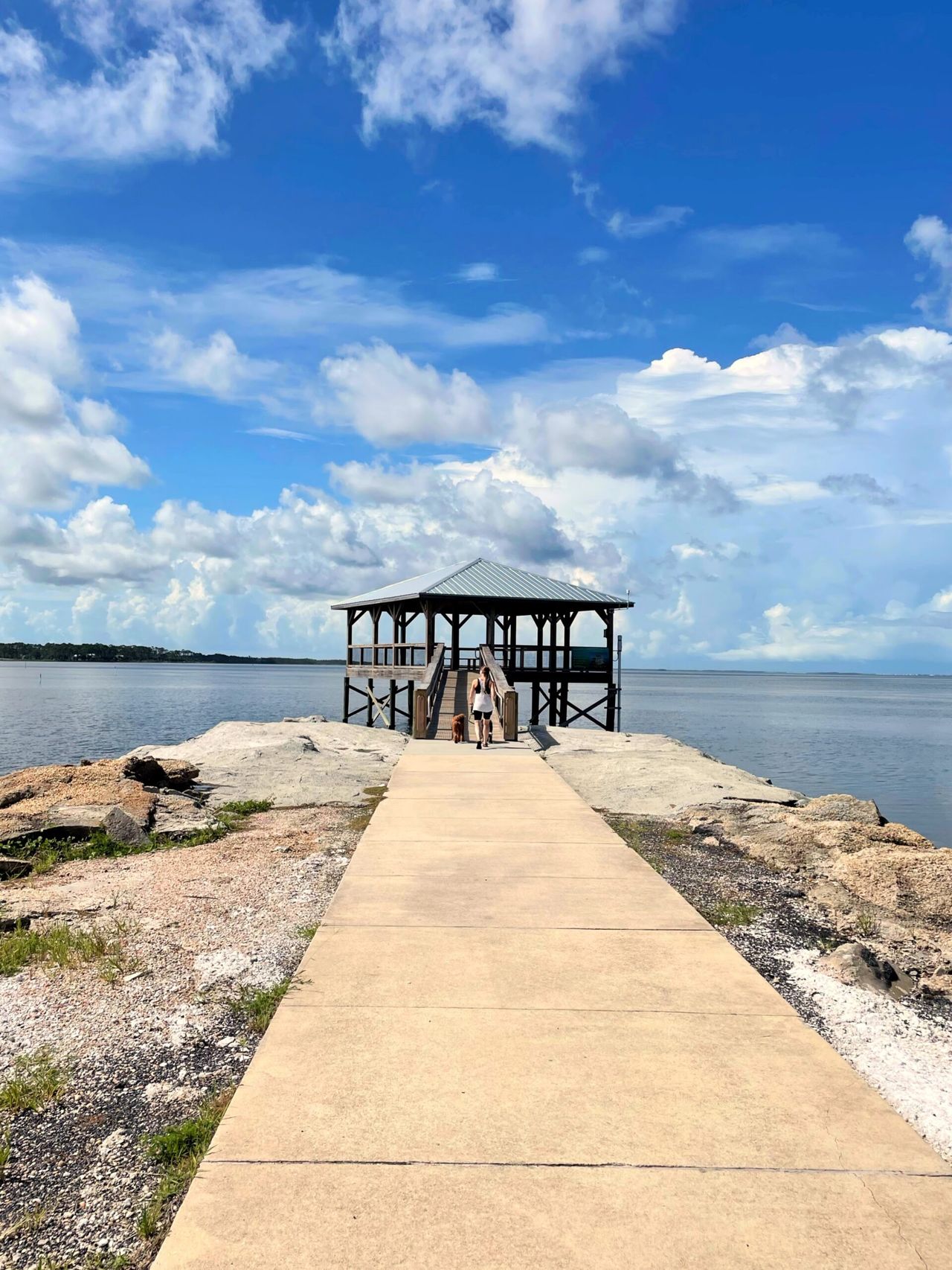 A large gazebo over the water. Holly and the dogs are centered walking on a path towards it.