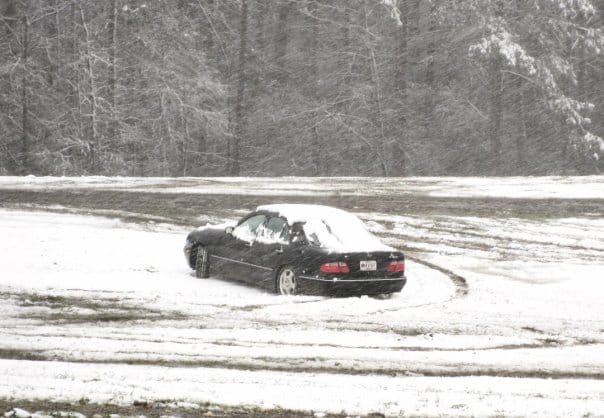 A black Mercedes sedan drifts in the snow.