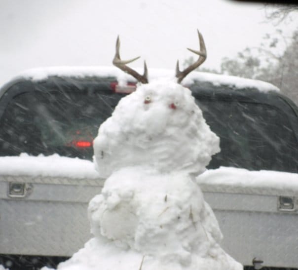 A snowman with antlers in the back of a pickup truck.