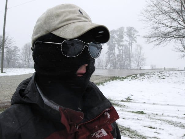 Andres with a ski mask, sunglasses and a hat out in the cold.