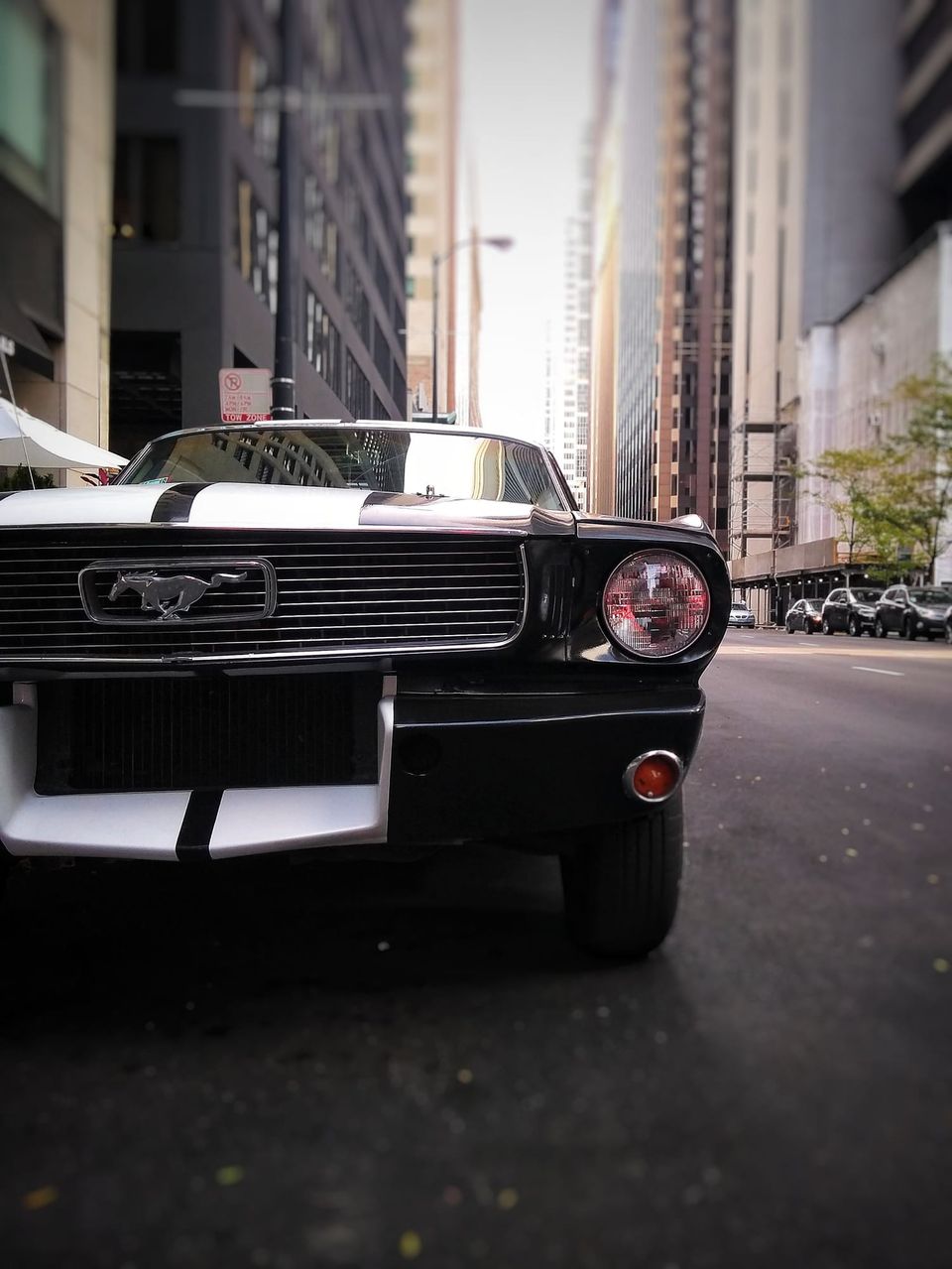 Front grille and headlight of a black classic Ford Mustang with white stripes parked on a downtown Chicago street