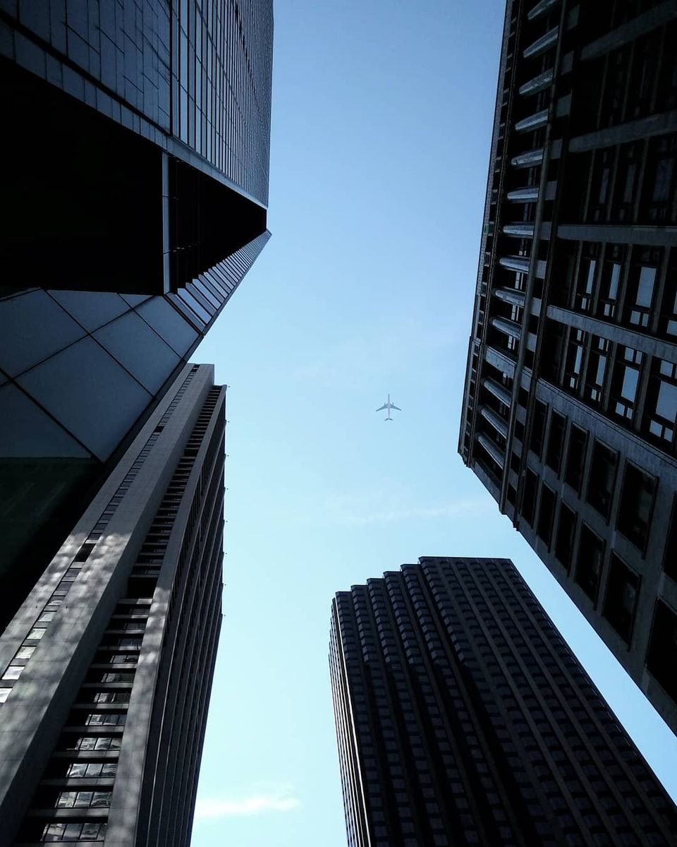 Looking up between four Chicago skyscrapers at a plane crossing a blue sky