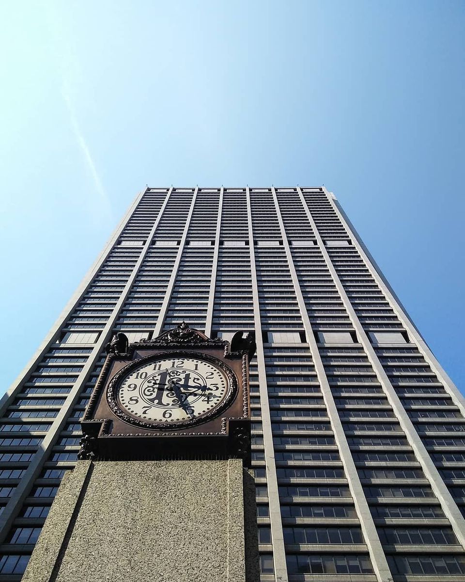 Ornate clock with a 1st logo on a pillar in front of a tall striped skyscraper