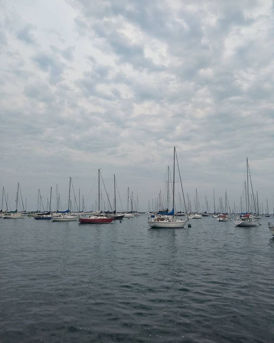Dozens of moored sailboats in a harbor under a cloudy sky