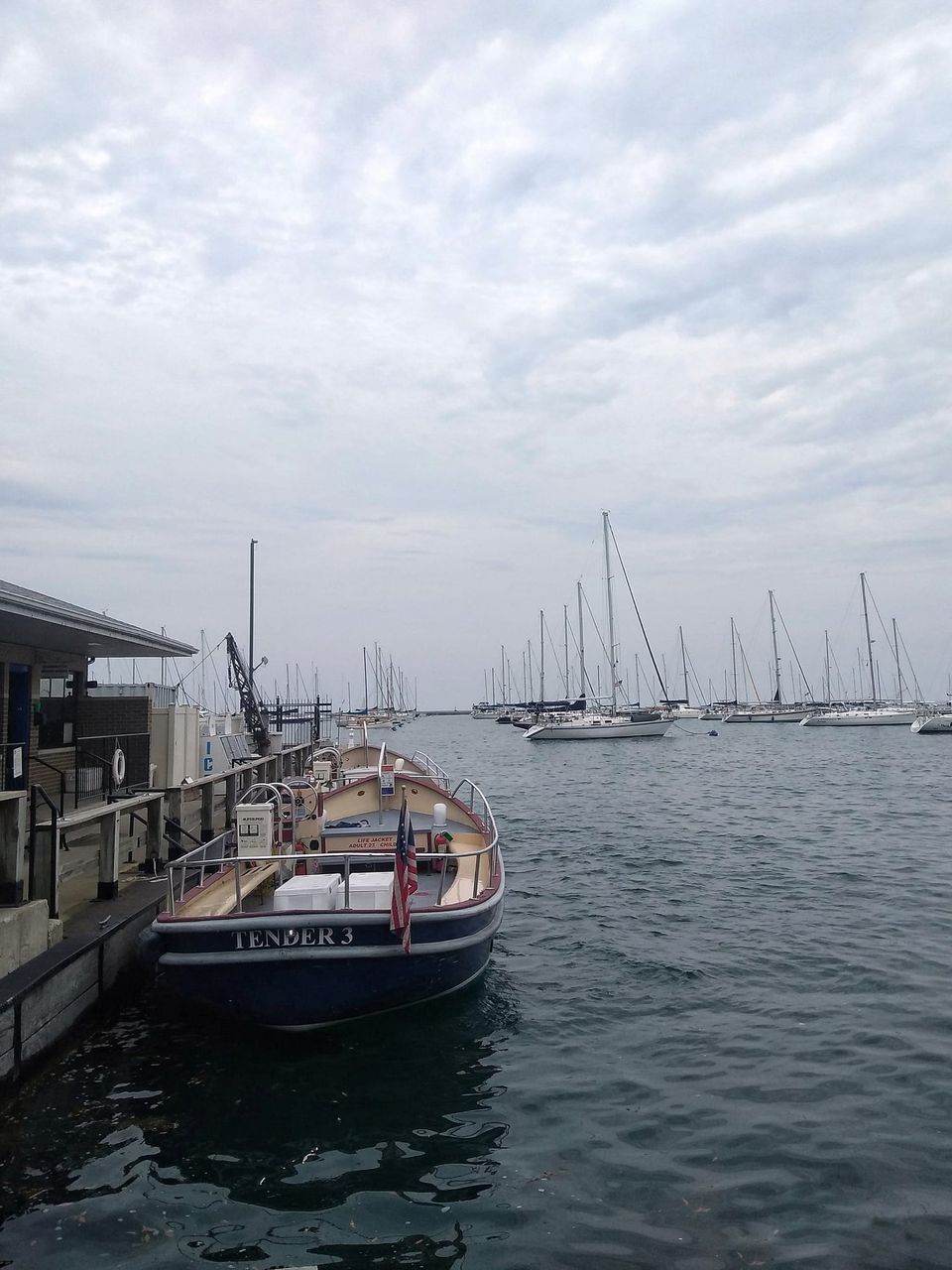 Navy boat named Tender 3 with an American flag docked beside a harbor full of sailboats