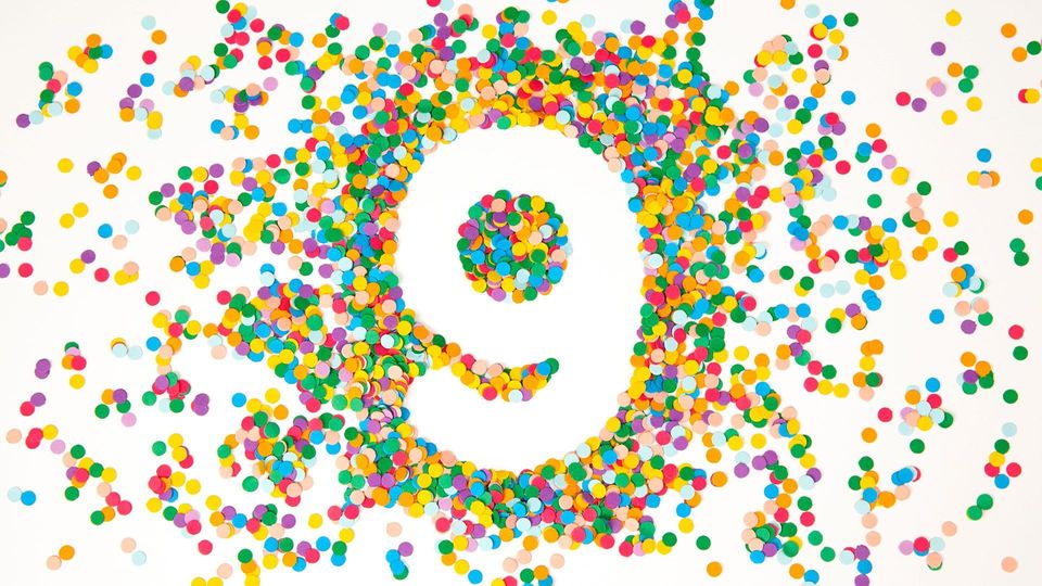 Number 9 formed from negative space in a burst of colorful paper confetti on white