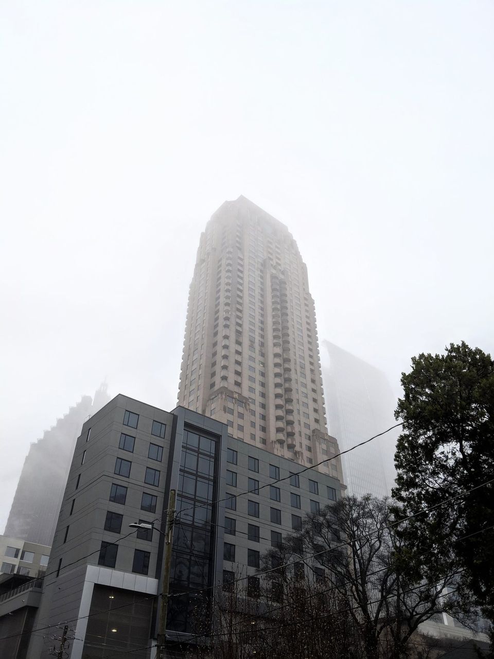Fog-shrouded high-rise tower rising behind a gray building in Atlanta