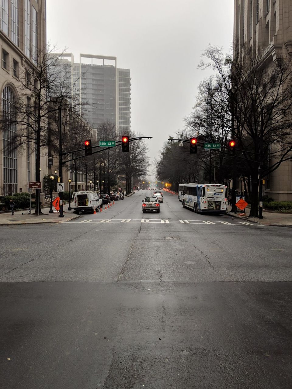 Wet empty intersection at 14th St NE in Atlanta with red lights, a bus and bare trees