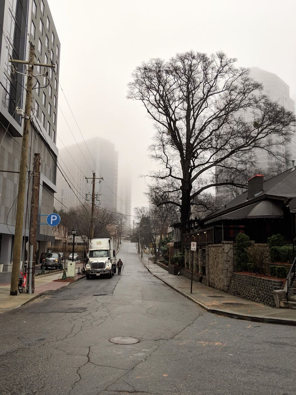 Foggy side street with a US Foods truck, bare tree and towers fading into mist