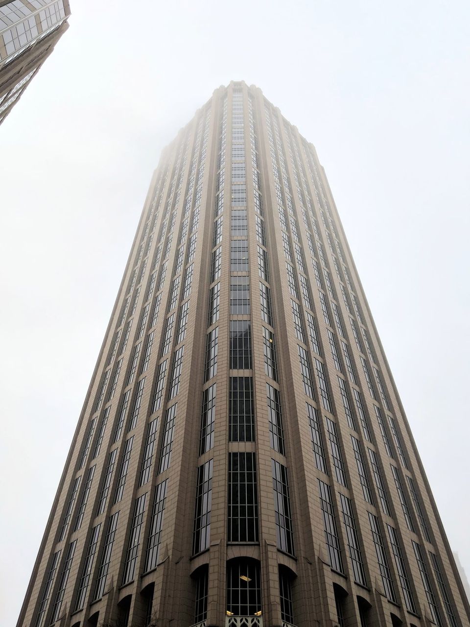Looking up at a tall beige skyscraper disappearing into fog