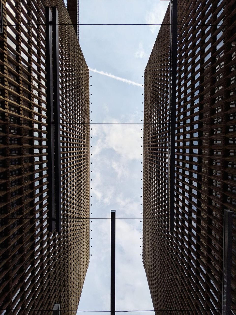 Looking up between two towers with grid-like concrete facades toward a cloudy sky