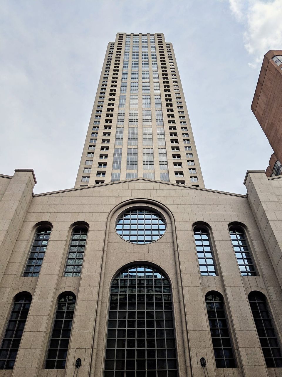 Tall beige skyscraper rising behind a stone facade with a round window and arched windows