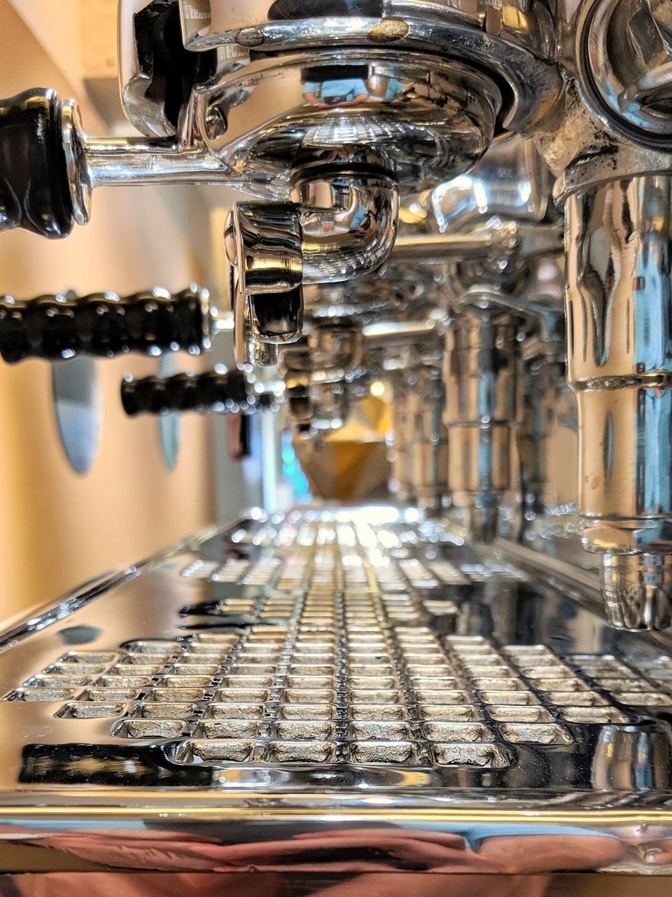 Low close-up of a chrome espresso machine's drip tray and group heads