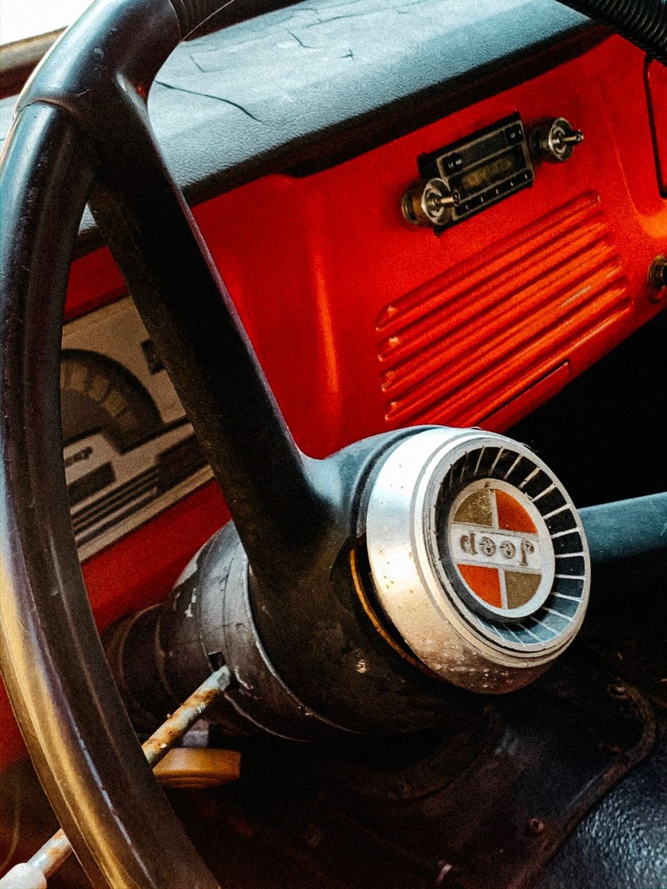 Worn black steering wheel with a Jeep horn button in front of a red dashboard