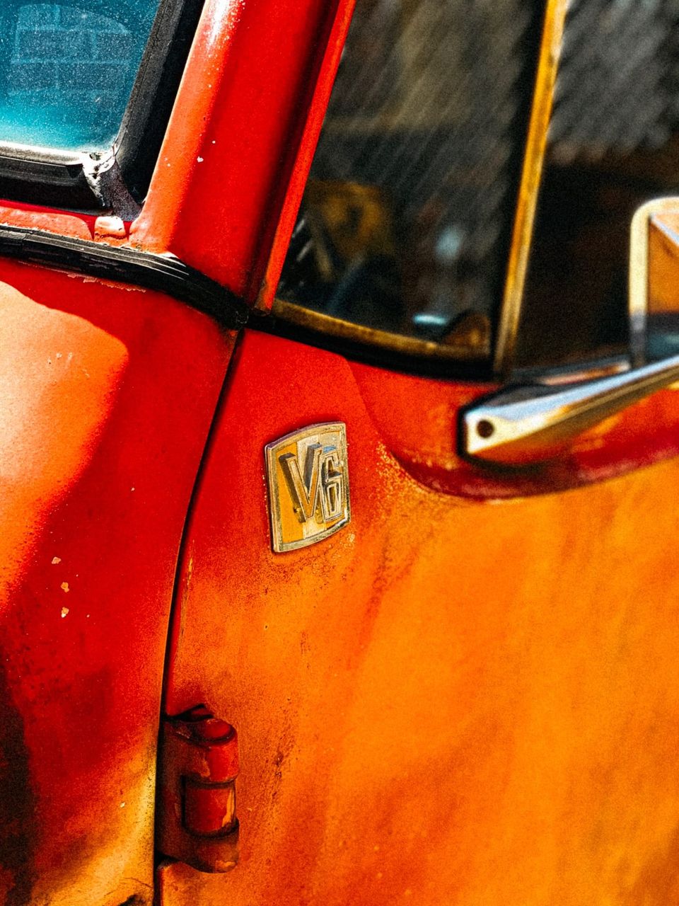 Close-up of a V6 badge on the sun-faded orange-red door of a vintage Jeep