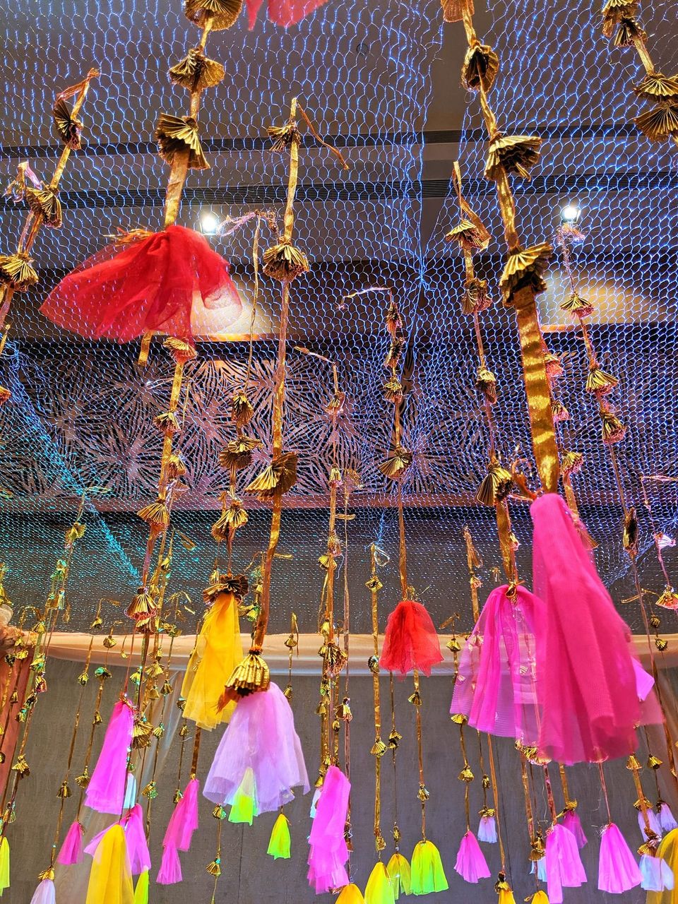 Gold ribbon garlands with pink, yellow and red tulle tassels hanging from a mesh ceiling