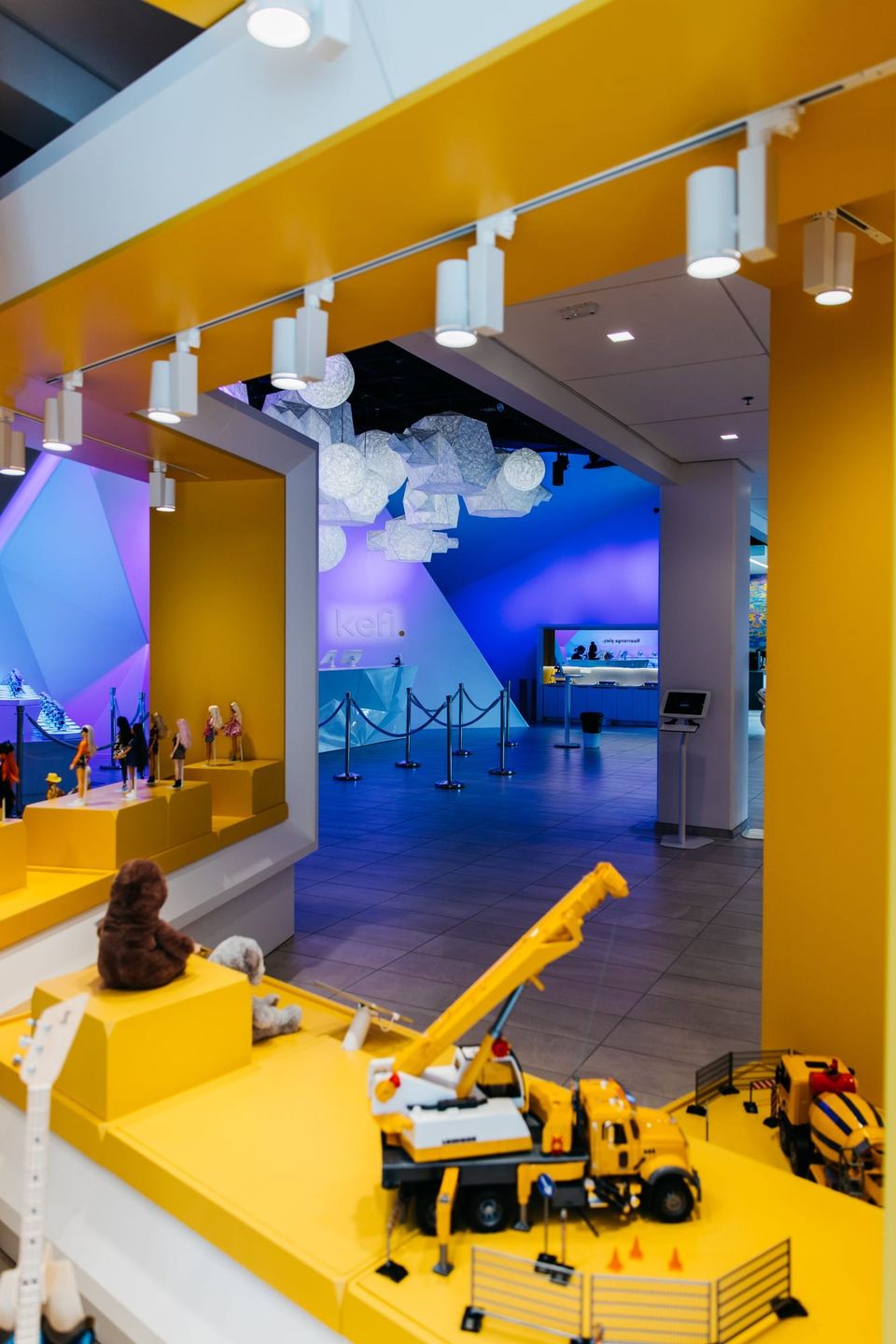 Kefi entrance with yellow toy displays of dolls and construction trucks leading to a purple-lit lobby