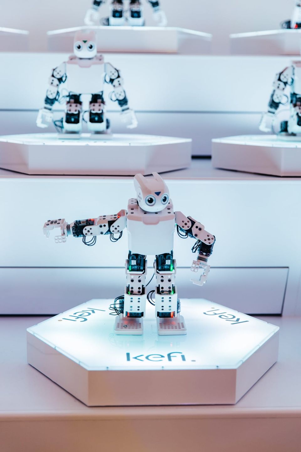 Small white humanoid robot on a glowing hexagonal Kefi pedestal with more robots behind