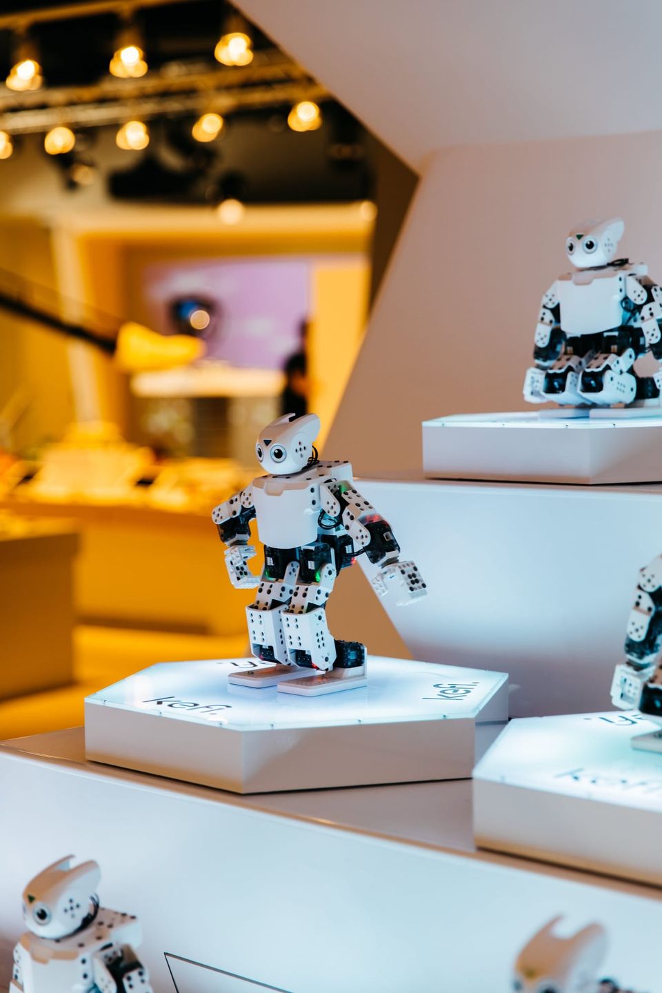 White robots posed on tiered glowing Kefi pedestals in a warmly lit store