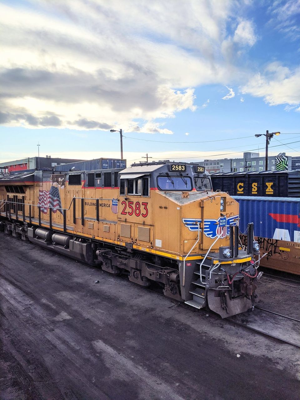 Yellow Union Pacific locomotive 2583 with an American flag beside CSX freight cars