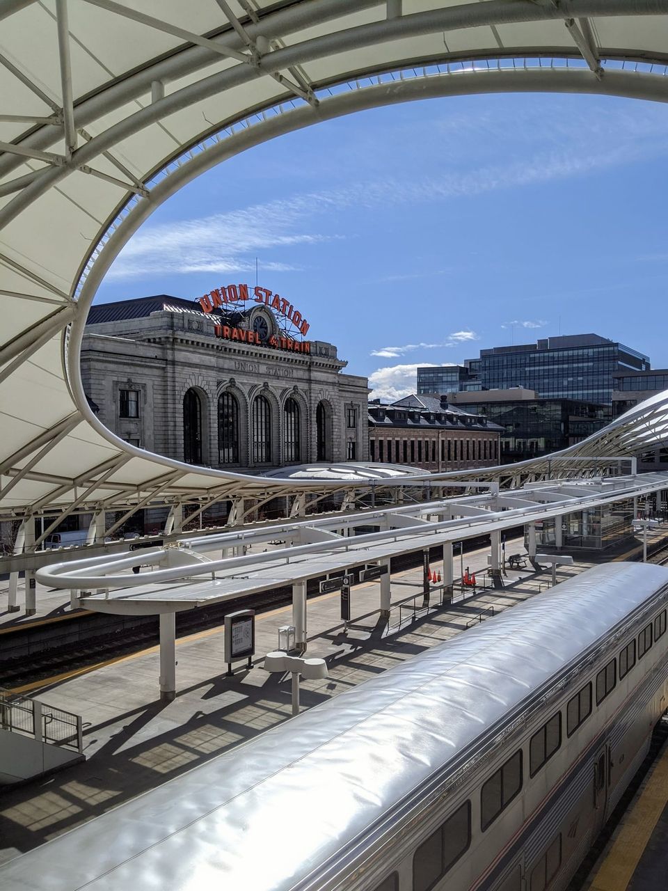 Denver Union Station's Travel by Train sign framed by the curved white canopy above an Amtrak train