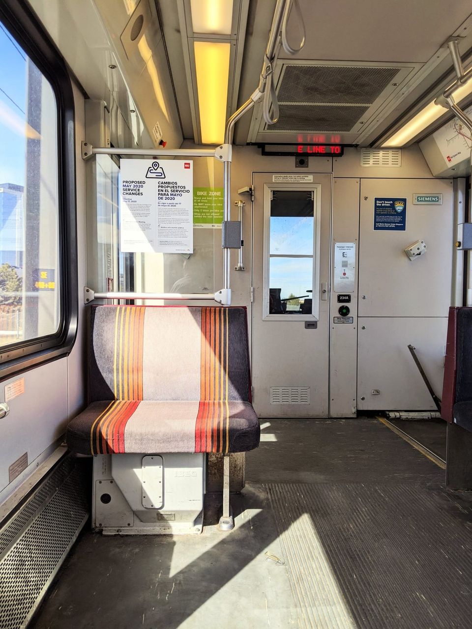 Empty light rail car with a striped seat, a May 2020 service changes poster and an E Line sign