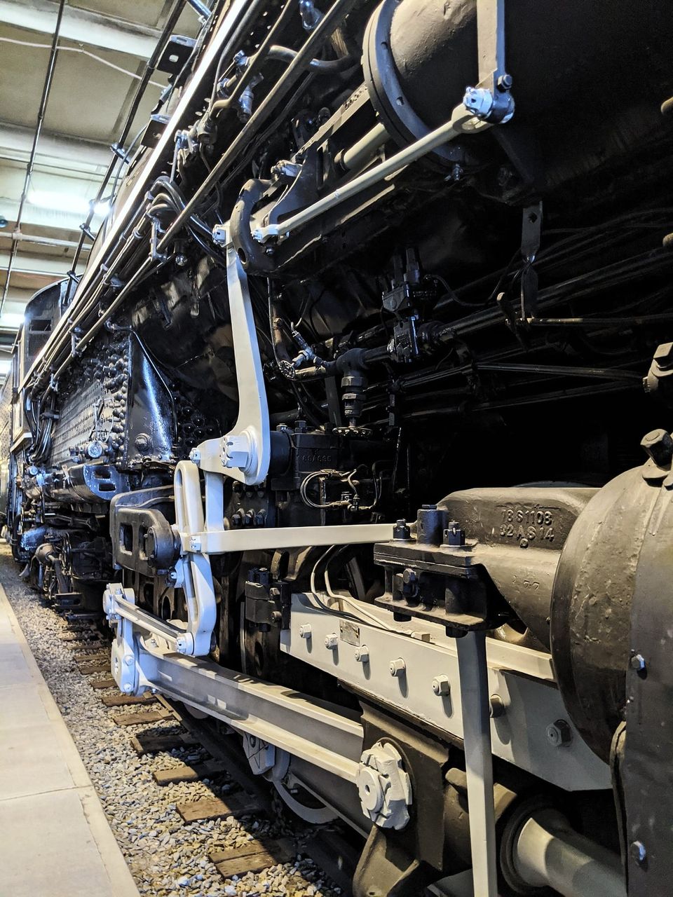 Low angle of a black steam locomotive's running gear and white-painted rods in a museum