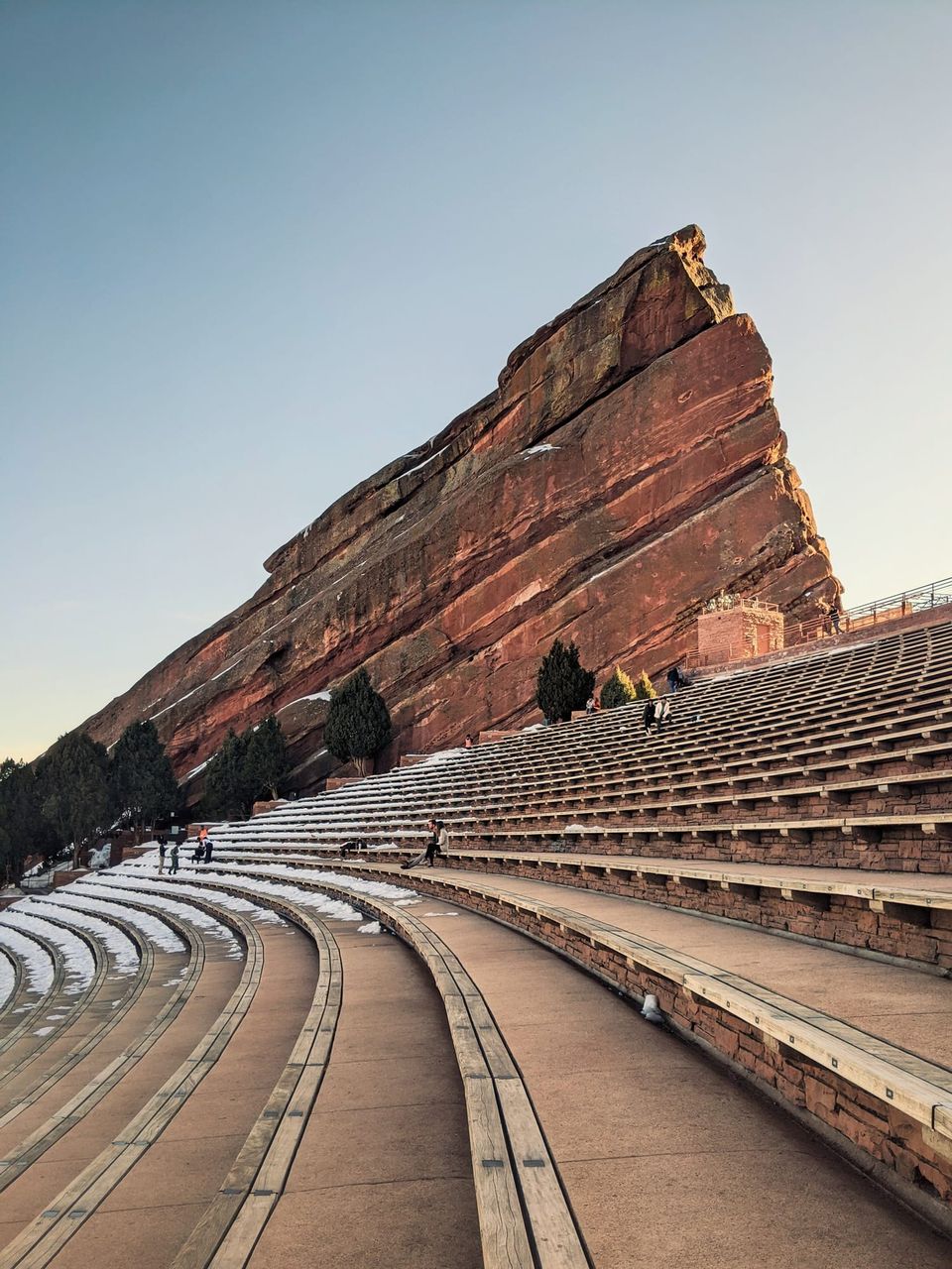 Red Rocks Amphitheatre's curved benches with light snow below a huge tilted red sandstone rock