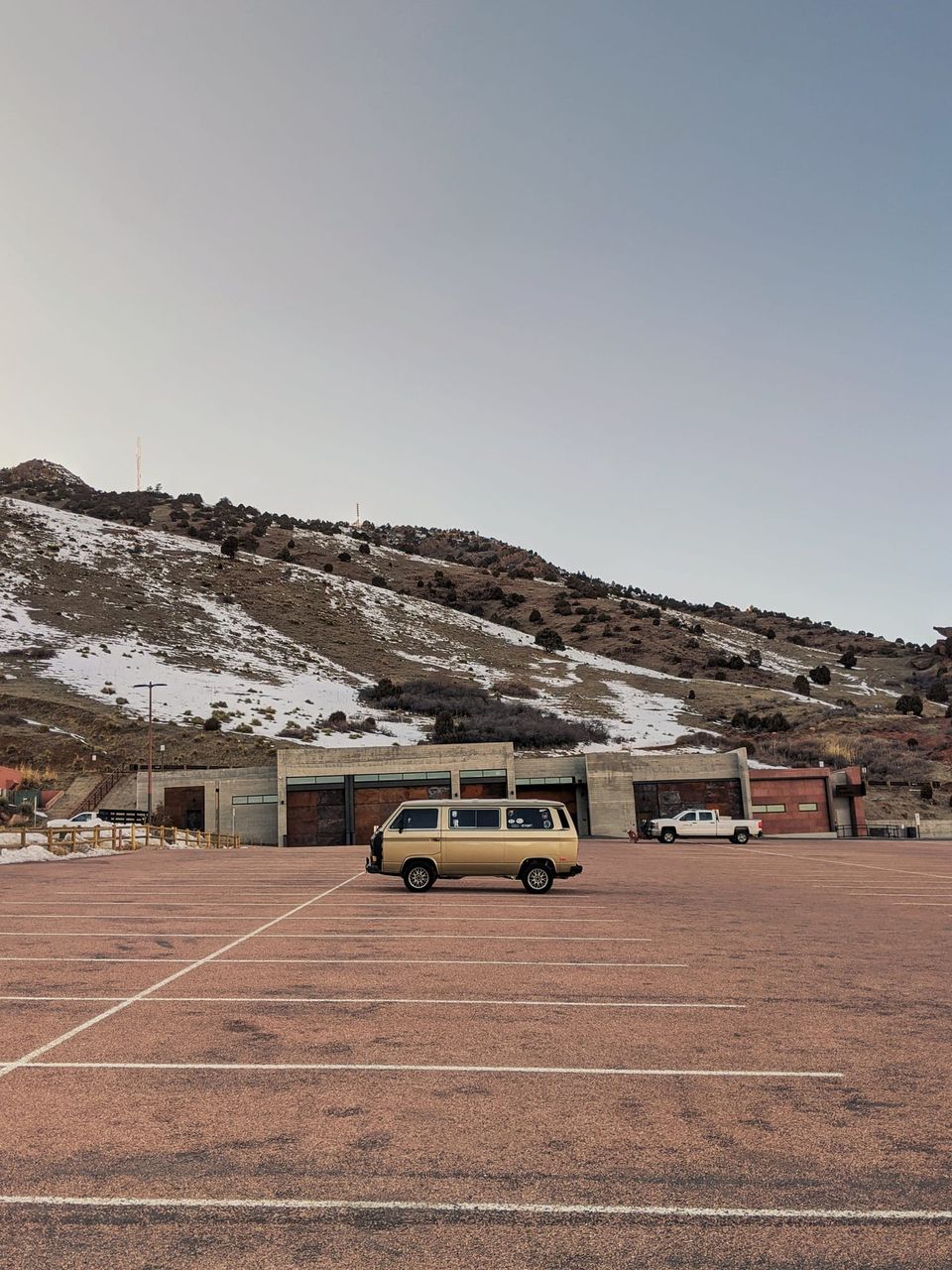 Gold vintage Volkswagen van alone in a red parking lot below a snowy hillside