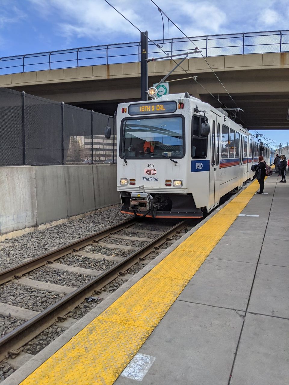 White RTD light rail train signed 18TH & CAL stopped at a platform under an overpass