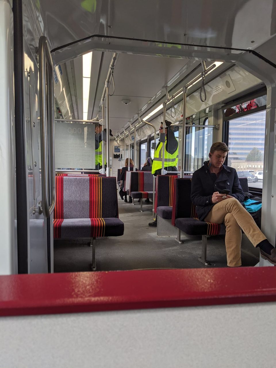 Inside an RTD light rail car with striped red and purple seats and a man in a peacoat on his phone