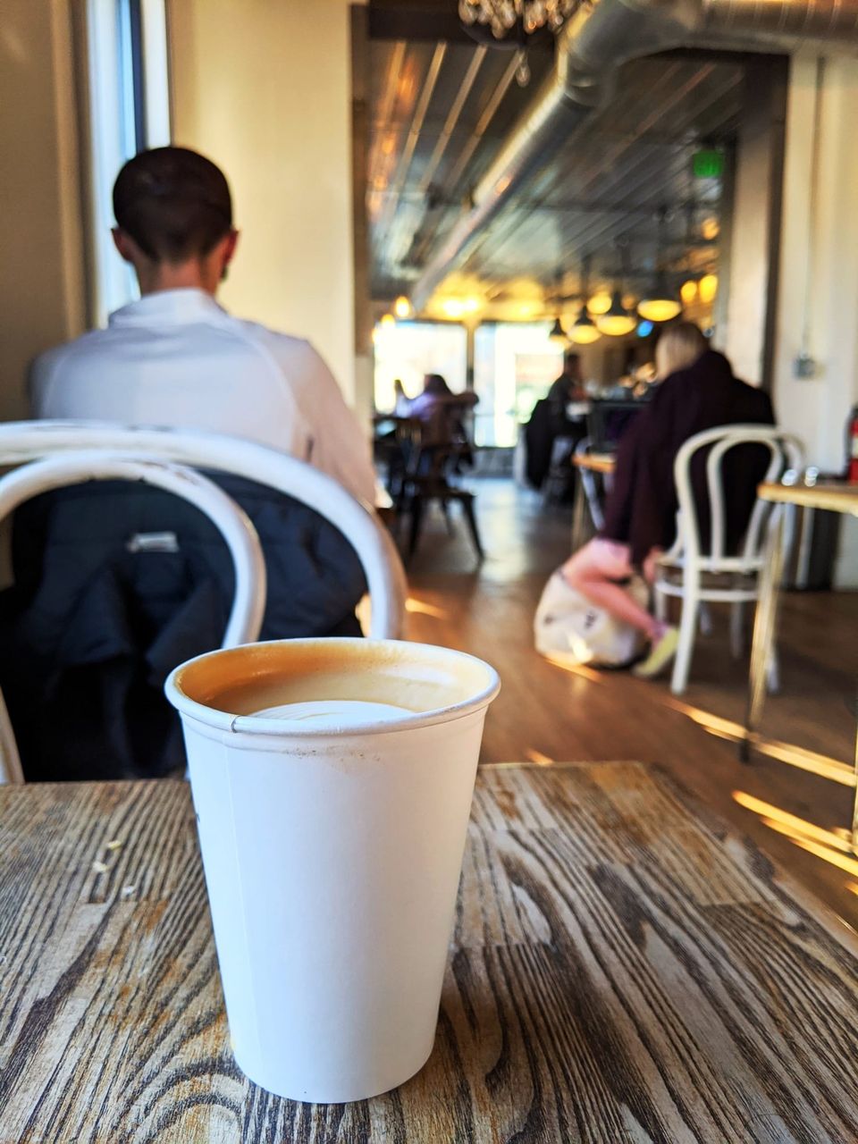 Paper cup of latte on a weathered wood table in a sunny café