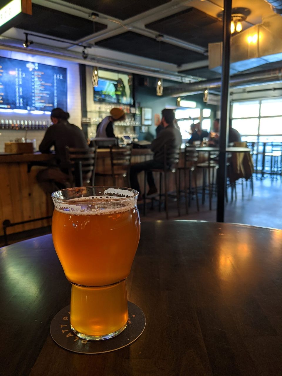 Glass of amber beer on a Platt Park Brewing coaster with a taproom bar blurred behind