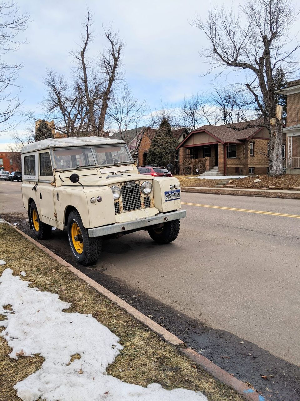 Cream vintage Land Rover with yellow wheels parked on a residential Denver street