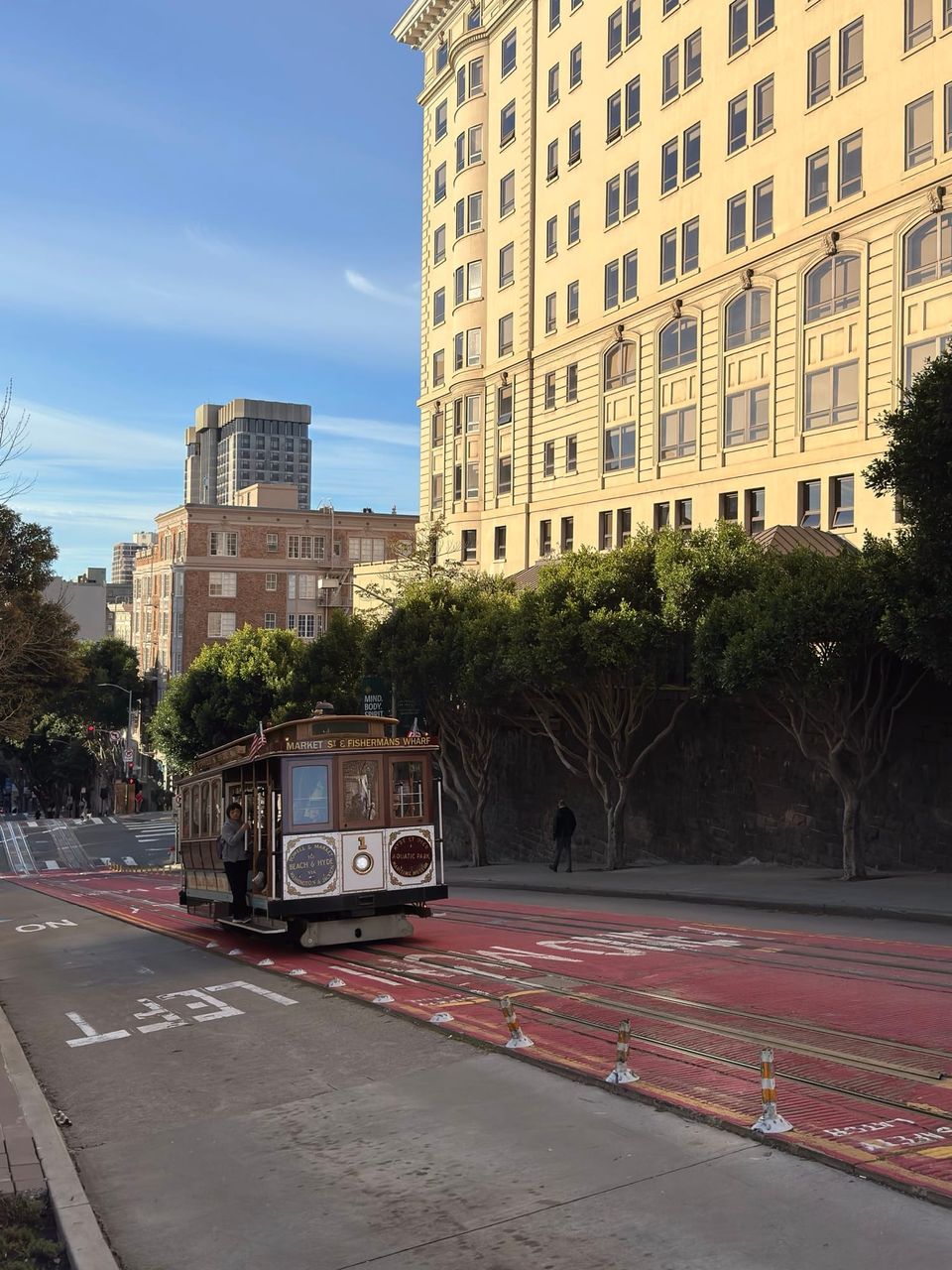 Powell and Hyde cable car climbing a red-lane street past a tall cream building in San Francisco