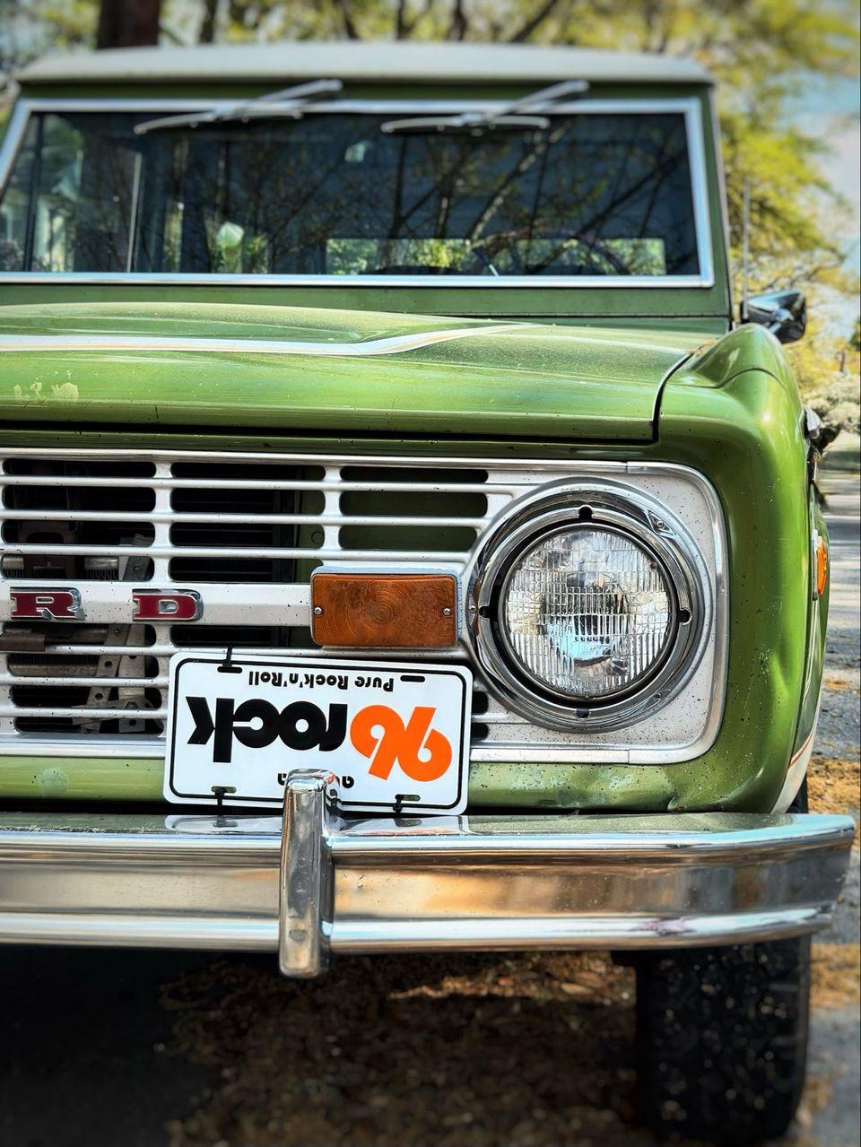 Close-up of a green vintage Ford Bronco grille and headlight with an upside-down 96 Rock Pure Rock'n'Roll plate