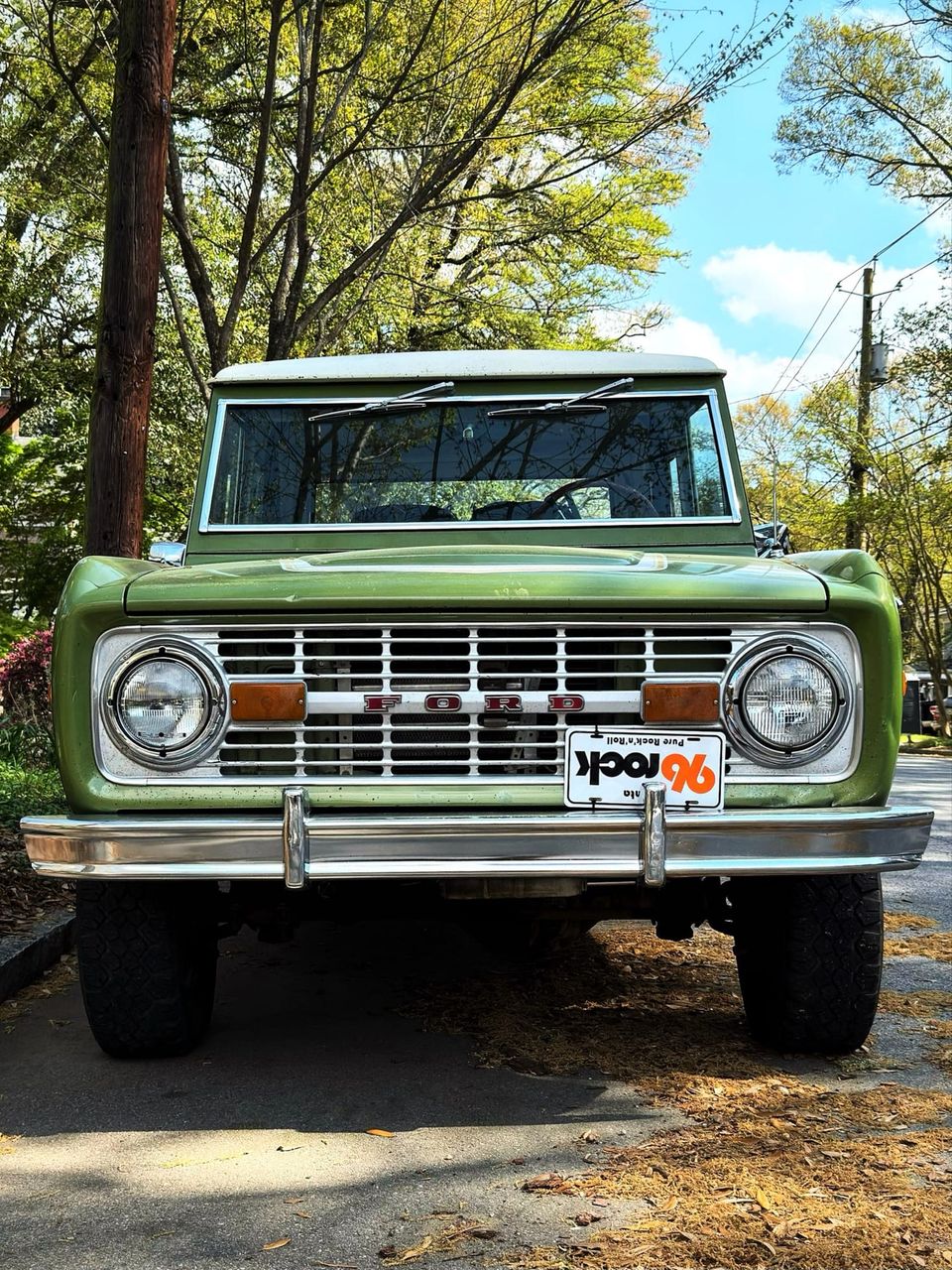 Head-on view of a green vintage Ford Bronco with a chrome bumper, round headlights and a 96 Rock plate
