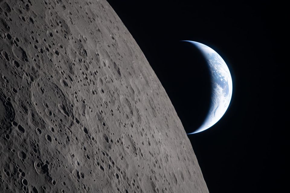 Cratered lunar surface in the foreground with a thin crescent Earth rising behind it