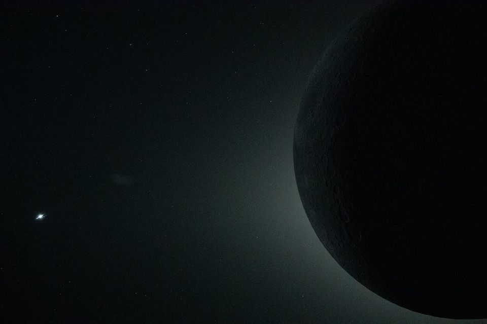 Dark silhouette of the Moon against faint starlight with a bright point of light at left