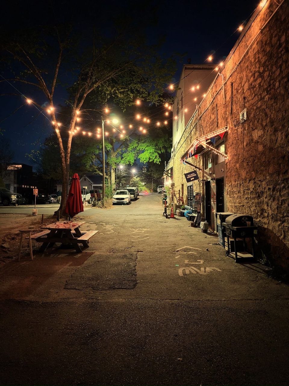 Night alley lit by string lights with a picnic table, red umbrella and a stone wall with an Atlanta Worldwide sign